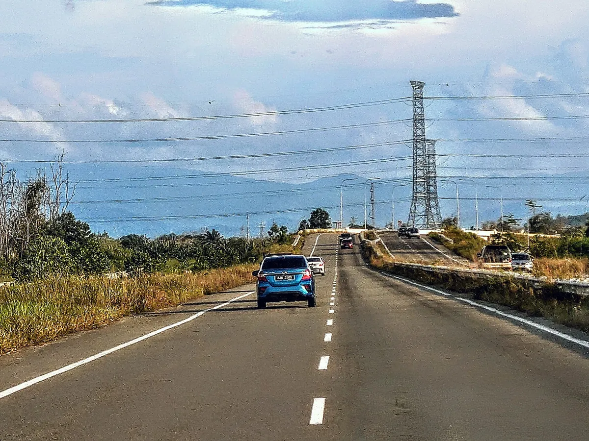 Cars on the new Pan Borneo dual carriageway near Papar, with a power pylon and hills behind