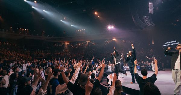 Hillsong Worship performing to a full arena with the crowd standing, hands raised